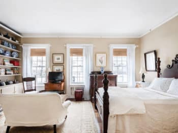 Bedroom with four poster bed, ivory bedding, area rug and 3 windows