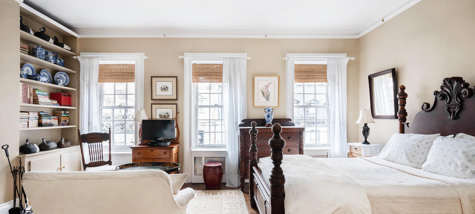 Bedroom with four poster bed, ivory bedding, area rug and 3 windows