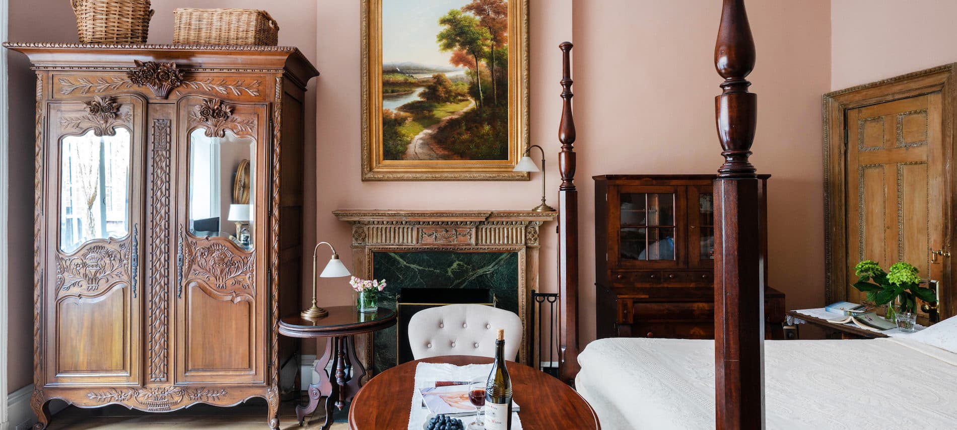 Bedroom with pink walls. Bed with tall headboard and four posters. Large Painting on Wall behind fireplace.