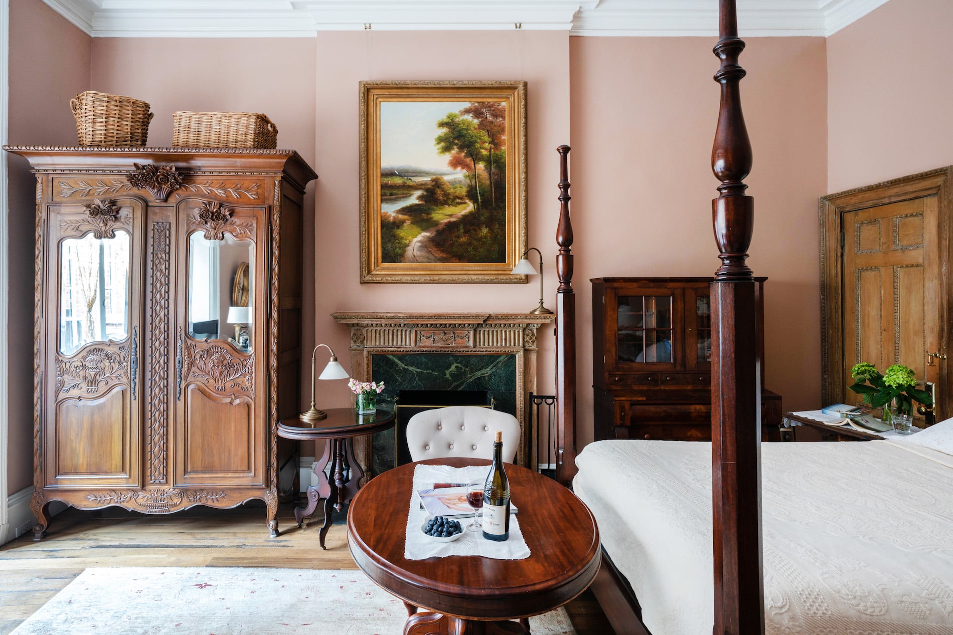 Bedroom with pink walls. Bed with tall headboard and four posters. Large Painting on Wall behind fireplace.