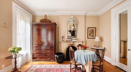 Bedroom with beige walls. Red area rug. Round Table and Chairs. Mirror above Fireplace Mantel. Brown armoire.