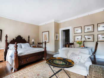 Dark Wood Four Poster bed with white bedspread, area rug. sofa and coffee table