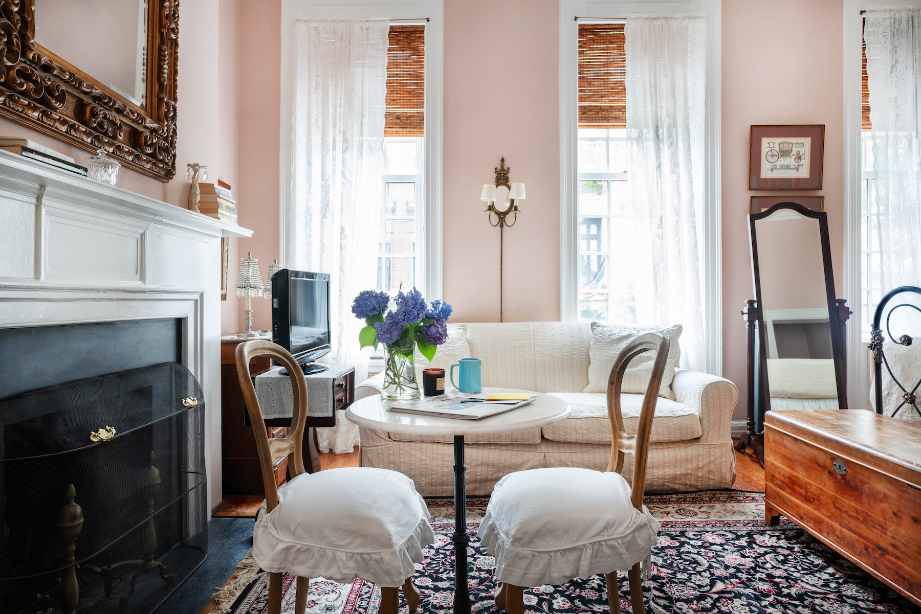 Room with tall ceilings. Pink Walls. Dark Rug. Beige Sofa. Small table with 2 chairs.