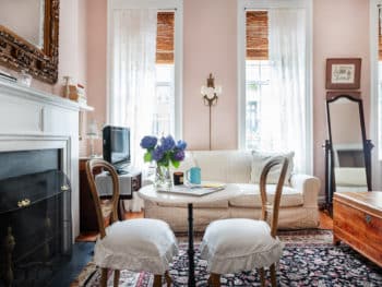 Interior room scene with sofa, small round marble table and two chairs with white seats. Black area rug. 3 windows.