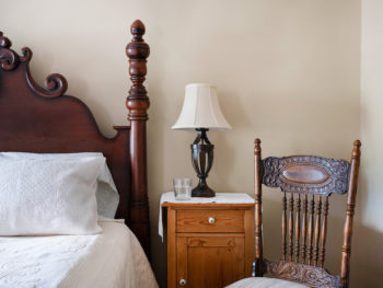 Dark wood bed with white bedding. Side table with lamp.
