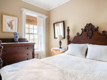 Dark wood bed with white bedding. Dark dresser next to window.