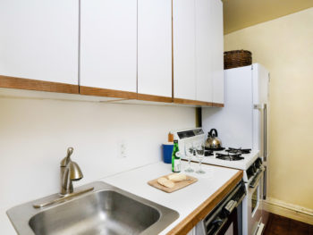 Kitchen with white cabinets. White countertop and stainless sink.