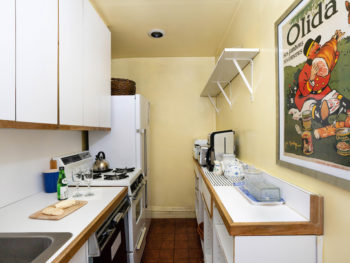 Kitchen with light yellow walls, white cabients and light brown floor.