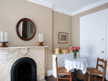 Wall with carved marble fireplace. Small round table with flowers.