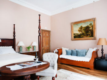 Bedroom with light pink walls. Daybed with blue pillows. Four poster bed. Area rugs on floor.