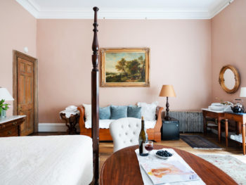 Large bedroom with two beds. Bureau with marble top and two green lamps. Blue and white pillows on small daybed.