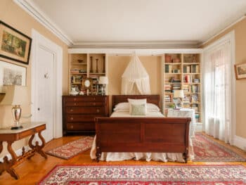 Dark Wood Sleigh Bed with mosquito netting, dark wood dresser next to bed, red oriental rug, beige walls