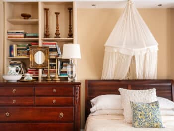 Dark Wood Sleigh Bed with mosquito netting, dark wood dresser next to bed, red oriental rug, beige walls