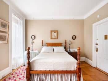 four poster bed with white cover. Red rug. Beige walls.