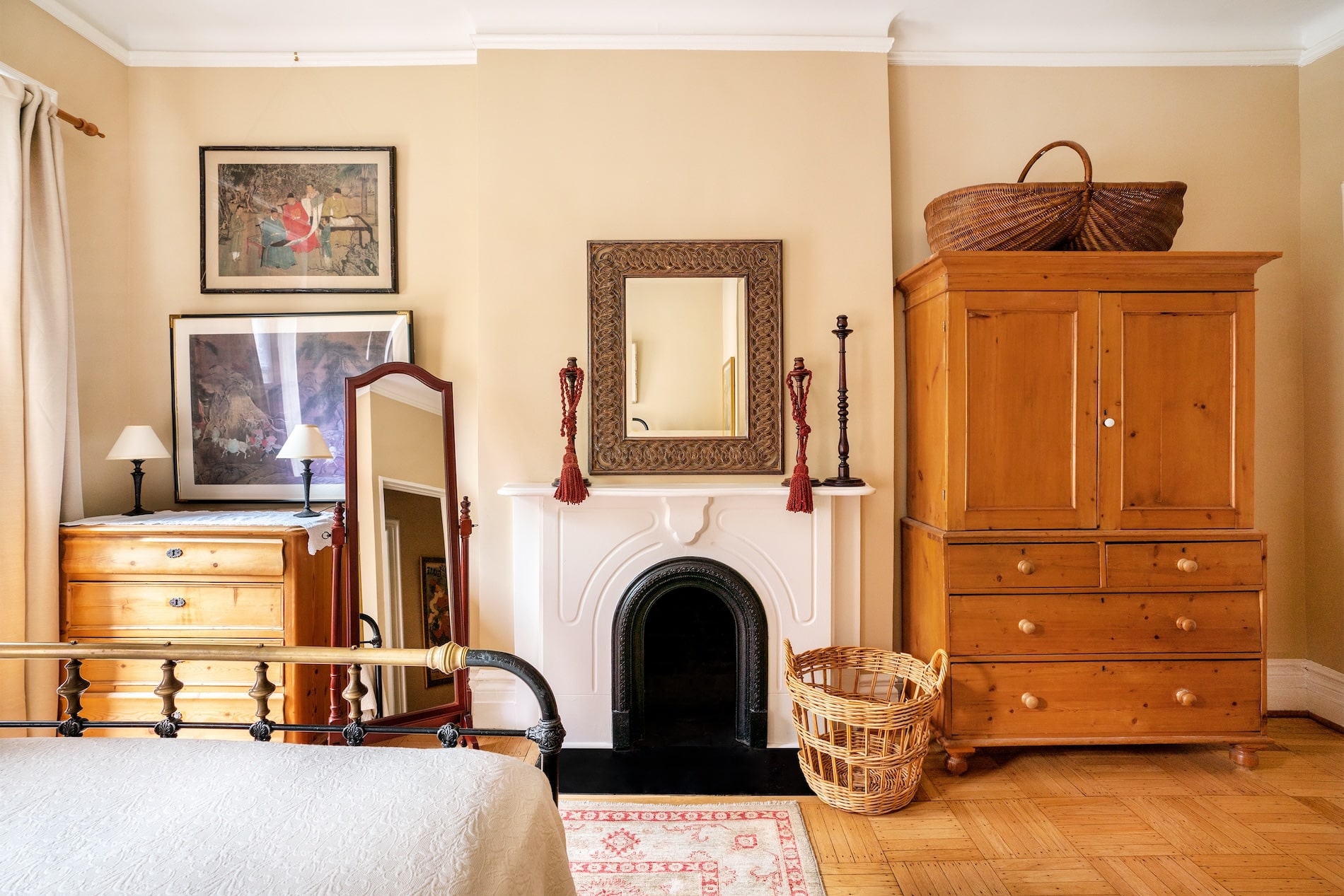 Bedroom with a white fireplace, mirror above and light pine bureau