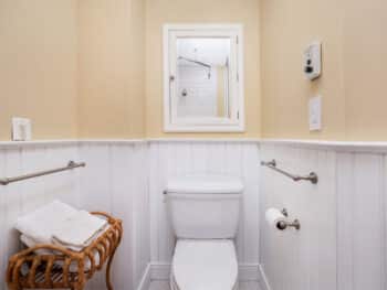 bathroom with beige upper walls and white wood walls on bottom. Toilet and mirror above.