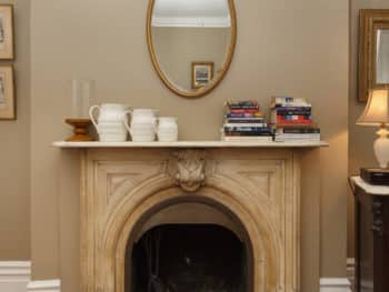 Marble Fireplace with oval mirror above. Taupe Walls.