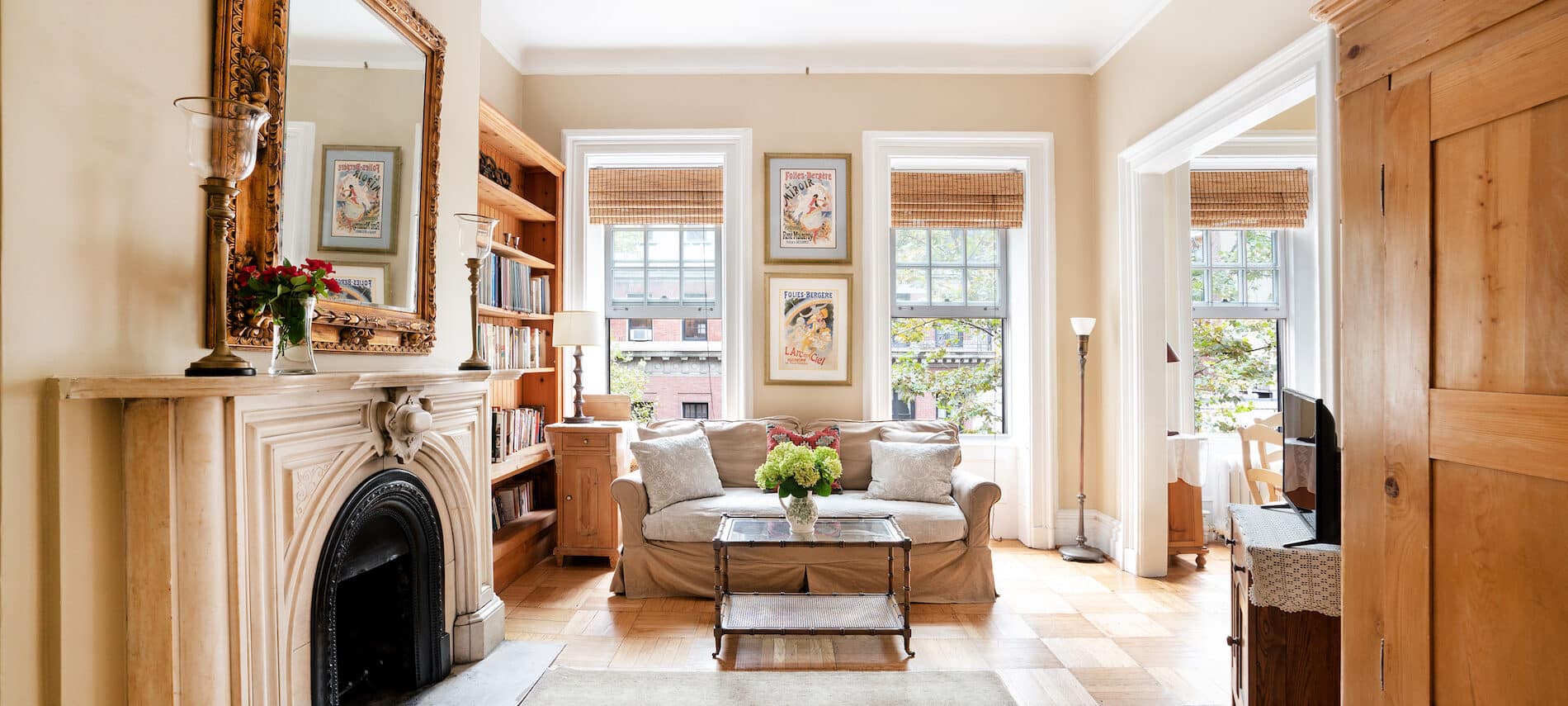 Well-lit sitting area with a tan & white sofa, glass coffee table, sitting chair, fireplace, bookshelves, & two tall windows