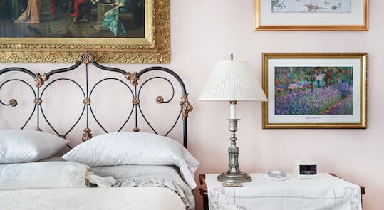 Bright bedroom furnished with a white-linen bed spread, bedstand with tall silver lamp. antique iron bed.