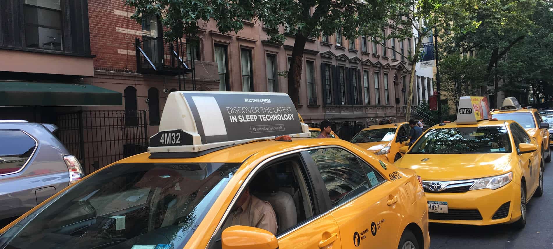 Two lines of yellow taxis in traffic outside a tall brick building